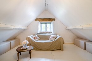 A cozy attic room with a sloped ceiling, a window, a sofa, a small table, and a vase with flowers. - 3 Bed in Llanvetherine (oc-g31918) (Llanvetherine)