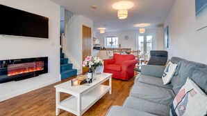 Un salon moderne avec une cheminée, un canapé, un fauteuil rouge et, au fond, un coin repas.
