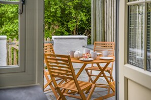 Conjunto de mesa e cadeiras de madeira montado num pátio com vista para o verde.