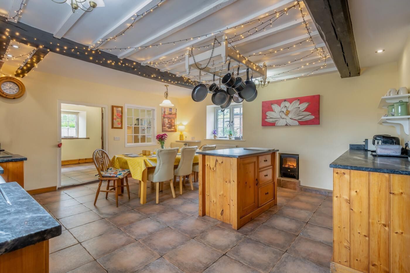 Une cuisine chaleureuse avec un îlot central en bois, des ustensiles de cuisine suspendus et des guirlandes lumineuses.