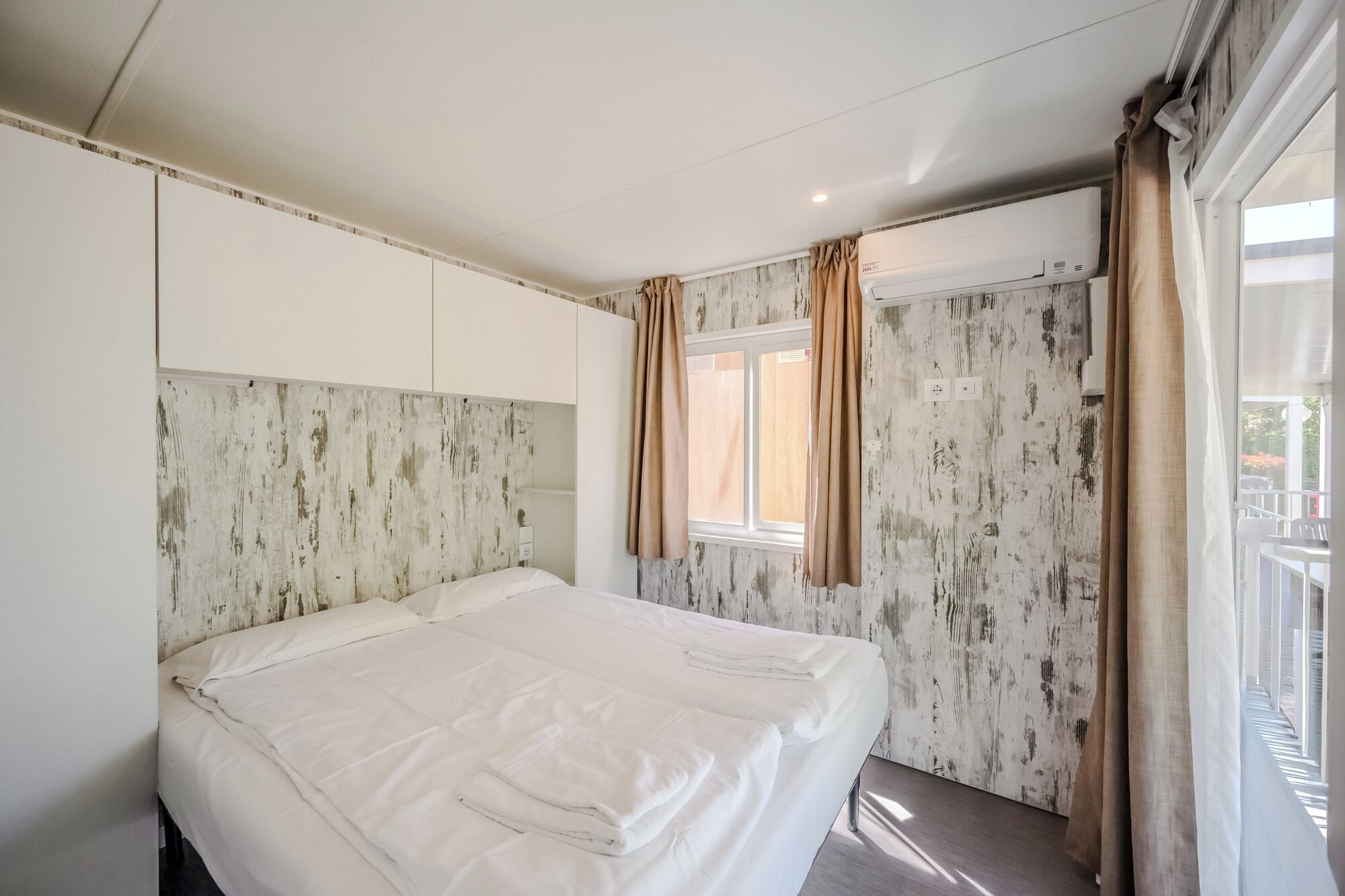 Une chambre d’hôtel avec un lit, une fenêtre avec des rideaux, un mur à motifs et un appareil de climatisation.