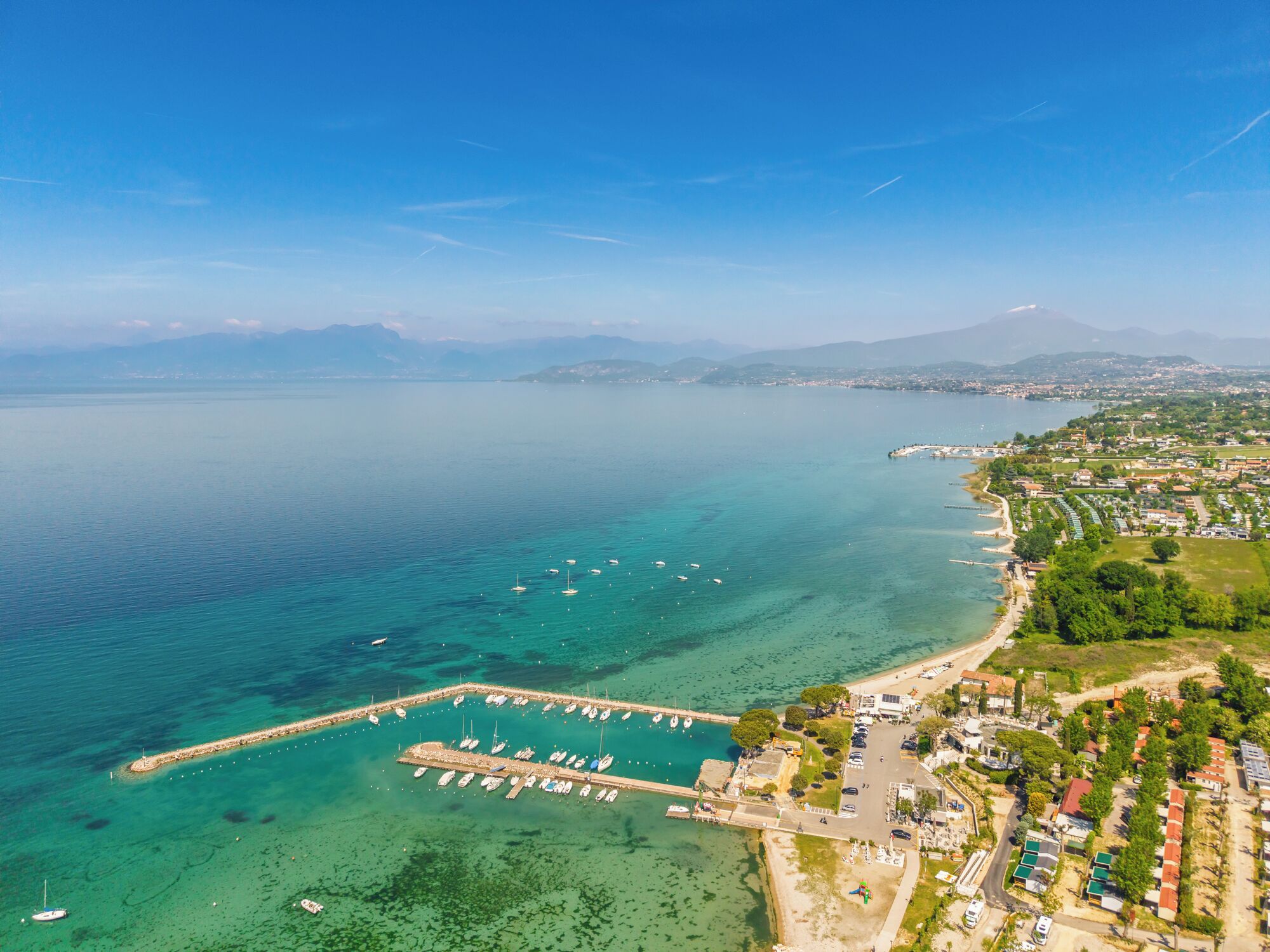 An aerial view of a coastal town with a marina, residential areas, and a mountain in the background.