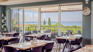 Um restaurante com mesas ao ar livre, janelas amplas e vista para um lago.