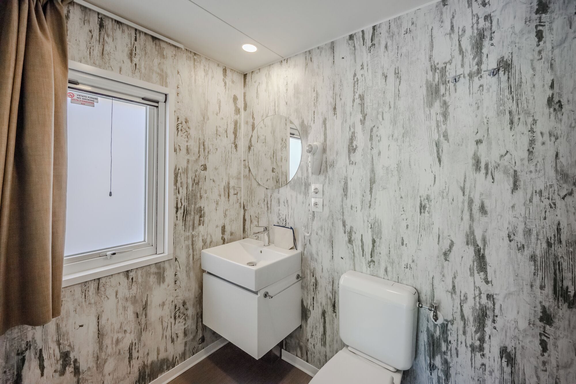 Un baño con lavamanos, inodoro y ventana con cortina.