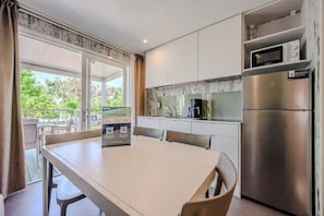 A modern kitchen with a stainless steel refrigerator, a microwave, and a coffee maker. There is a dining table with chairs and a view of the outdoors through a glass door. - Hotiday Lazise Garda (Pacengo)