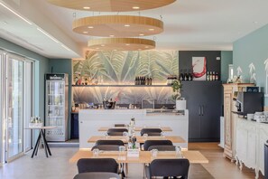 A modern bar area with a central counter, seating, and a decorative wall with leaf patterns. - Hotiday Lazise Garda (Pacengo)