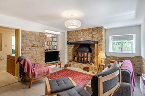 Ein gemütliches Wohnzimmer mit Kamin aus Stein, einem Fernseher und einem Bücherregal.