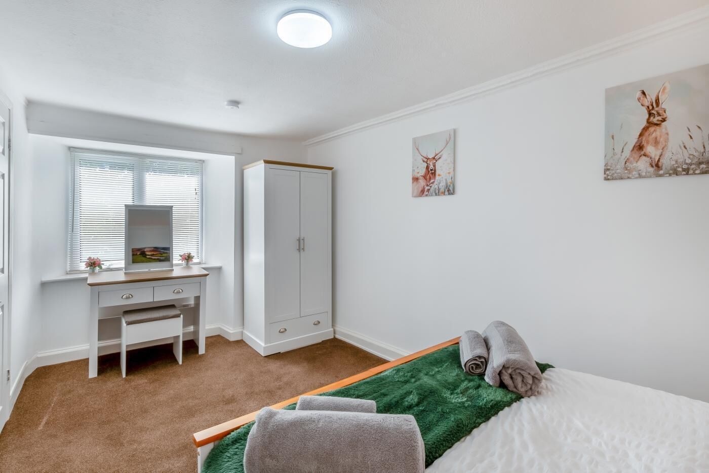 A bedroom with a bed, a desk, a wardrobe, and two wall art pieces.