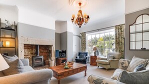 A cozy living room with a fireplace, comfortable seating, a television, and a large window with curtains. - 4 Bed in Bamburgh (oc-gd1264) (Bamburgh)