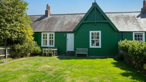 A green house with a white door, a small porch, and a lawn. - 2 Bed in Bamburgh (oc-gd1345) (Bamburgh)