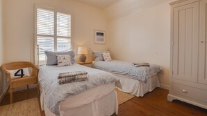 A bedroom with two beds, a wicker chair, a wardrobe, and a window with blinds. - 2 Bed in Bamburgh (oc-gd1345) (Bamburgh)