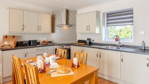 Una cocina moderna con gabinetes blancos, horno empotrado, extractor de acero inoxidable y una ventana con persianas.
