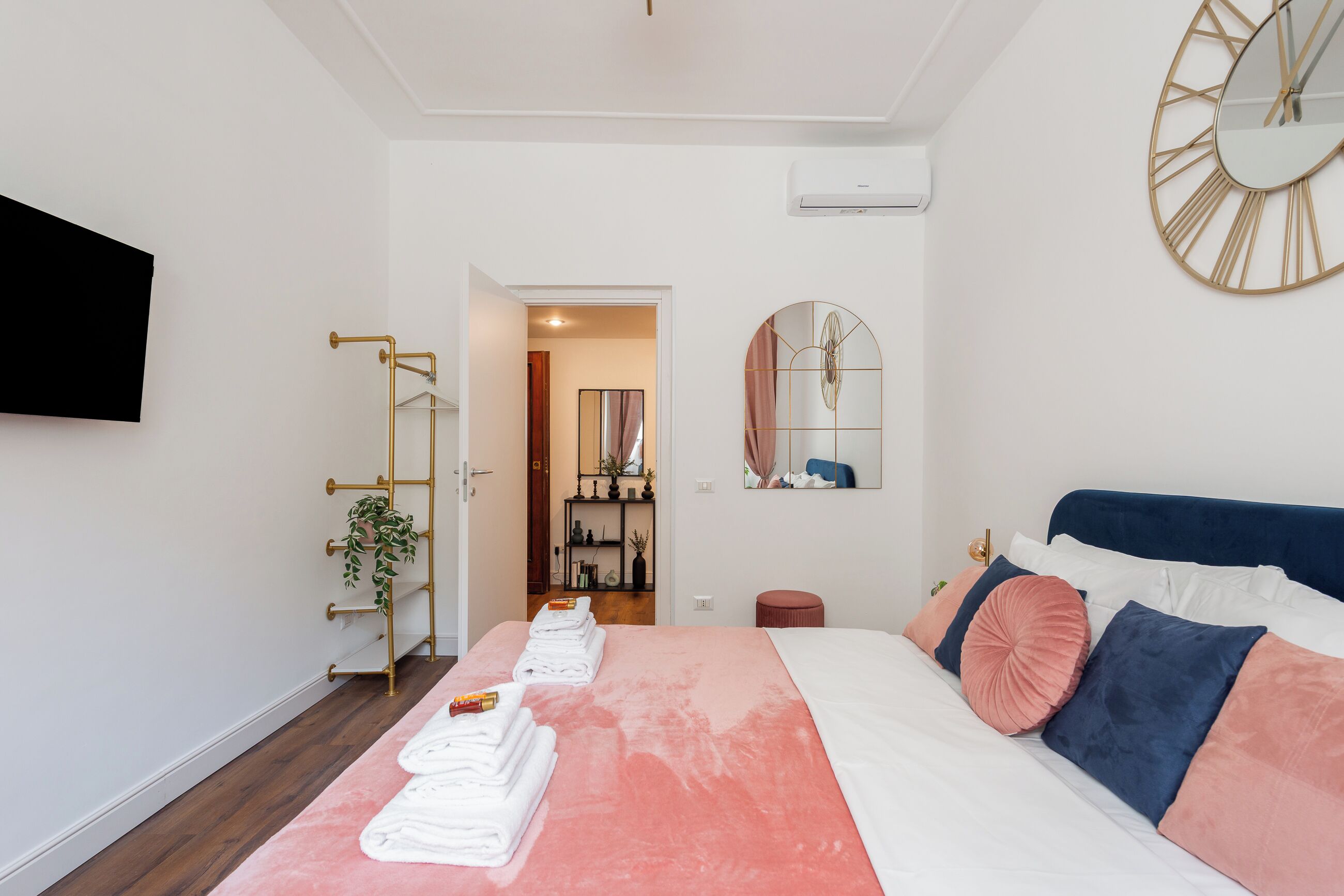 A modern bedroom with a bed, a TV, a mirror, and a plant.