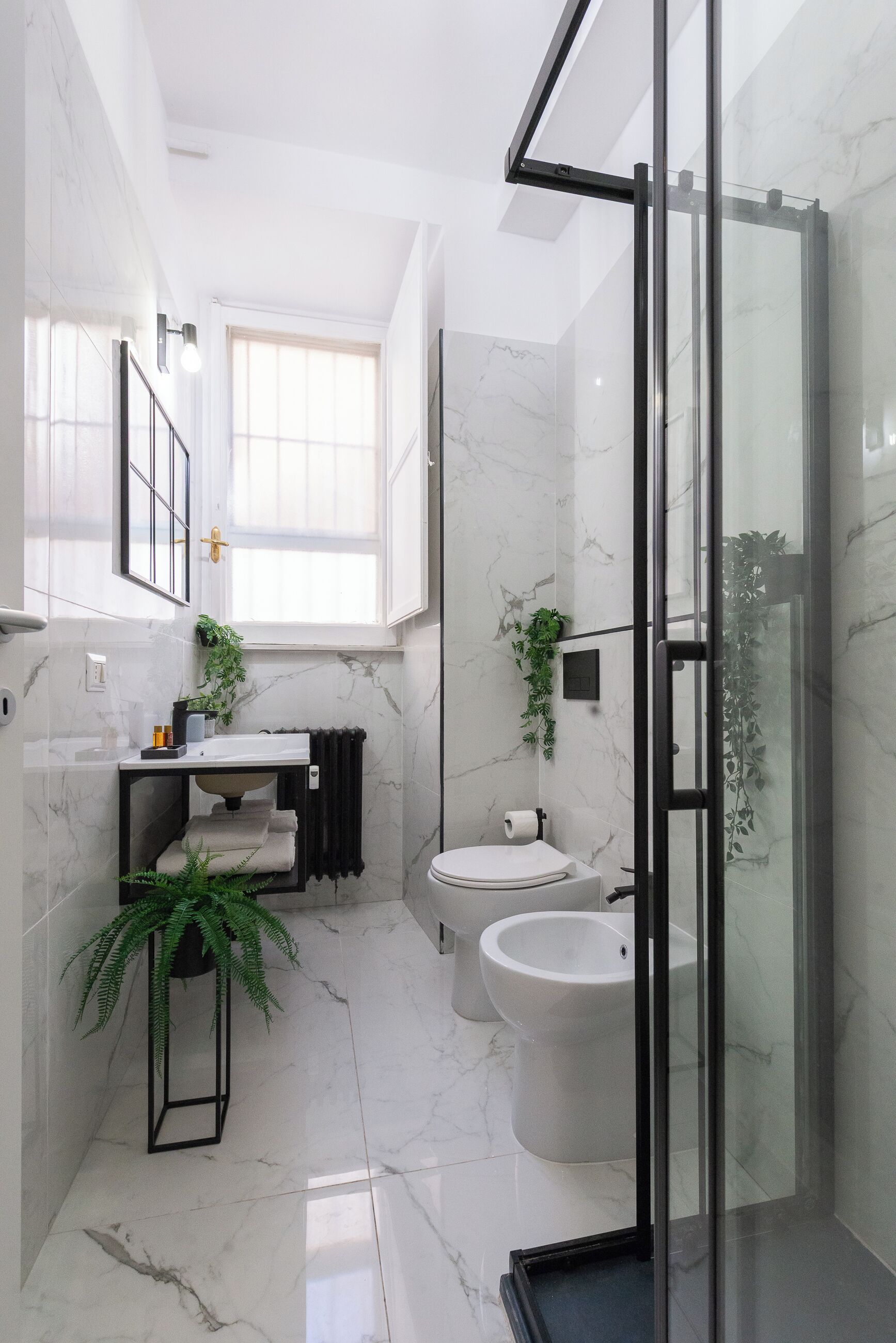 Un bagno moderno con doccia vetrata, pavimento in marmo, lavandino bianco e un water.