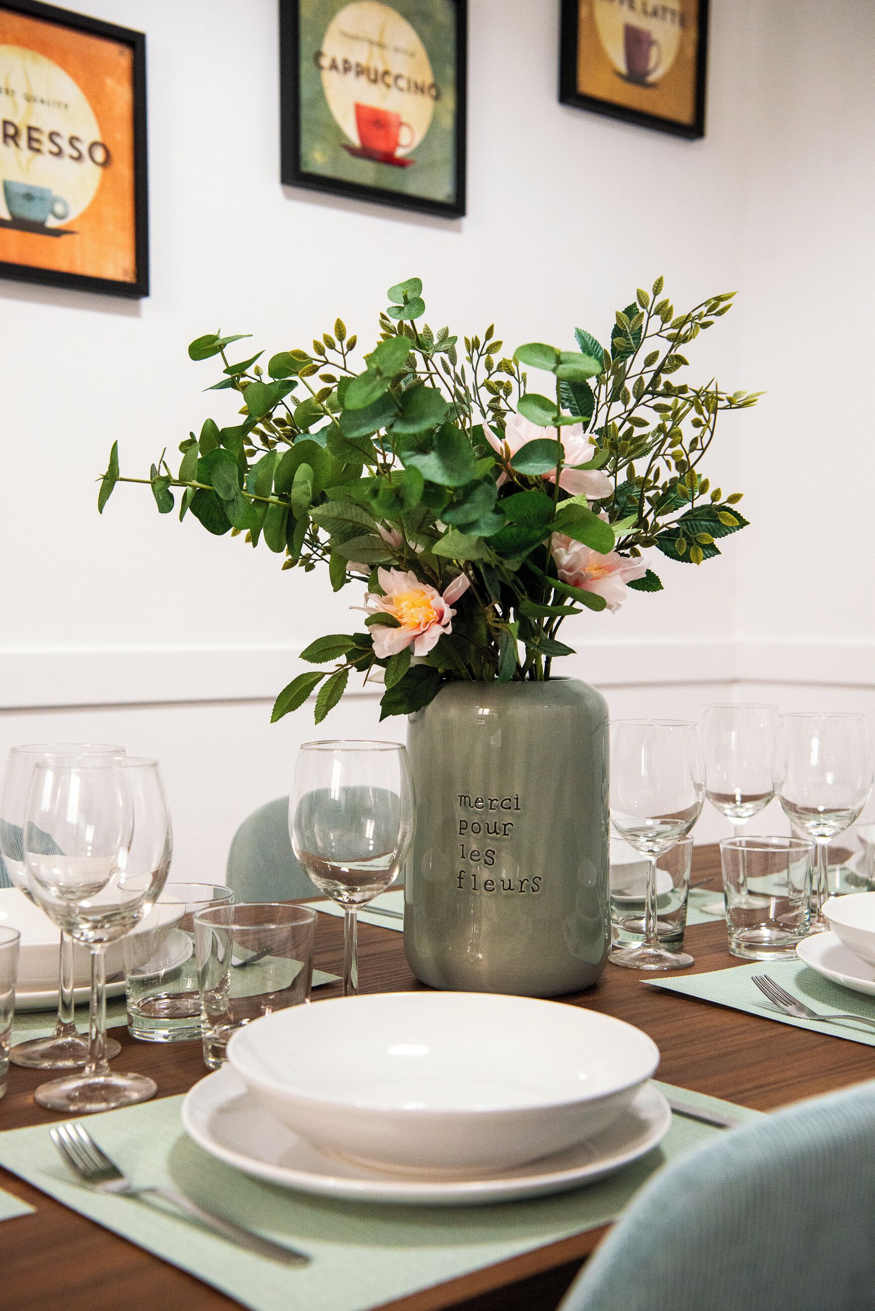 A dining table set with plates, glasses, and a vase with flowers.