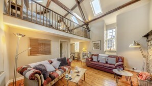 Un loft spacieux avec de hauts plafonds, des poutres apparentes, une grande fenêtre et un coin salon confortable avec deux canapés et une table basse.
