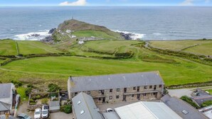 A coastal property with a stone building, a grassy field, and a lighthouse in the background.