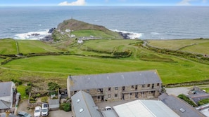 A coastal property with a stone building, a grassy field, and a lighthouse in the background. - 1 Bed in St. Just (oc-h31976) (Cape Cornwall)