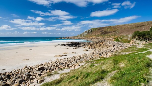 A beach with a rocky shoreline, a clear sky, and a distant view of the ocean.