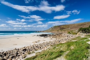 A beach with a rocky shoreline, a clear sky, and a distant view of the ocean. - 1 Bed in St. Just (oc-h31976) (Cape Cornwall)