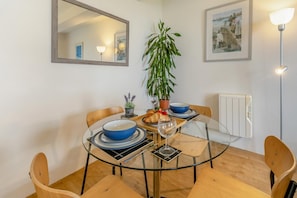 A dining area with a round glass table, four chairs, a potted plant, a framed picture, and a radiator. - 1 Bed in St. Just (oc-h31976) (Cape Cornwall)