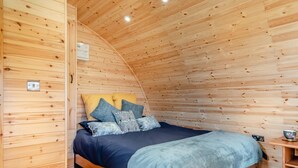 A wooden interior with a curved ceiling, a bed with multiple pillows, and a small wooden table with a bowl. - 1 Bed in Sandown (oc-h31917) (Newchurch)