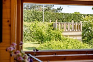 Une cabane en bois avec une fenêtre donnant sur un jardin, délimité par une clôture en bois et caractérisé par une végétation luxuriante.