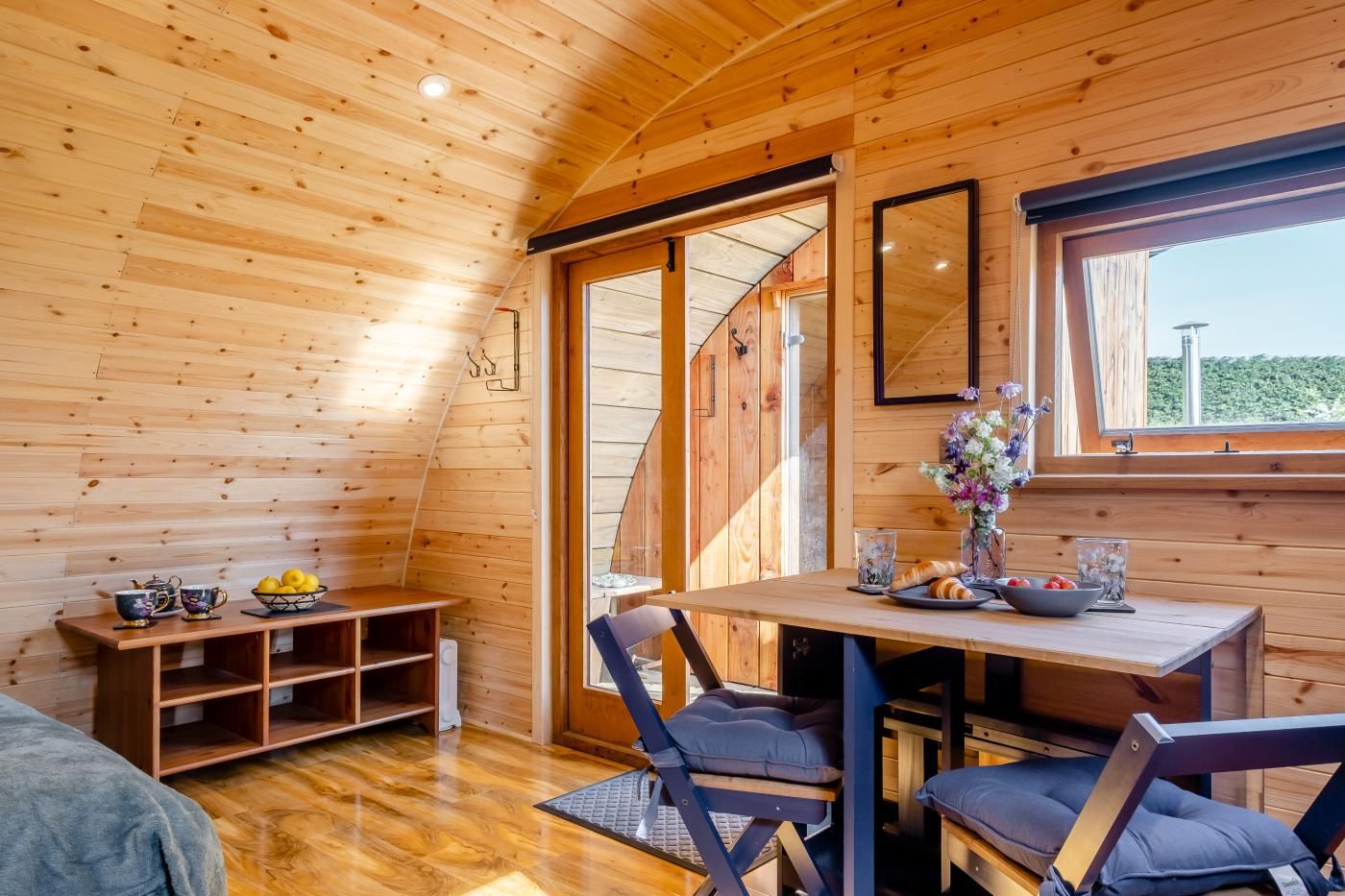 A wooden interior with a dining table, chairs, a bench, and a window with a view.