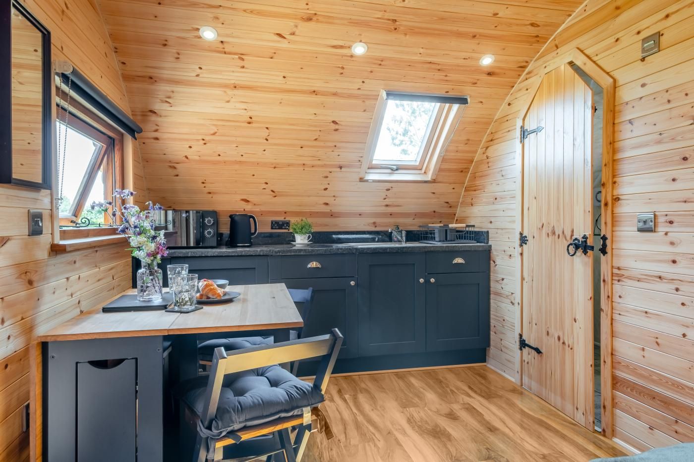 Une cuisine compacte avec un coin repas, des murs en bois, une lucarne et un four encastré.