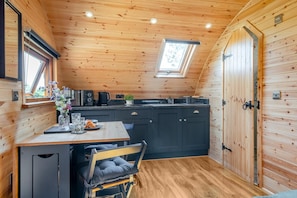 Une cuisine compacte avec un coin repas, des murs en bois, une lucarne et un four encastré.
