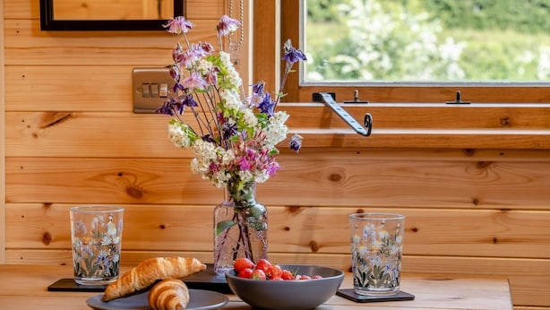 Een houten interieur met een raam, een bloemenvaas, een schaal aardbeien, twee glazen en twee croissants op een tafel.