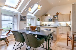 A modern kitchen with skylights, a dining area with a table and chairs, and wooden cabinets. - 2 Bed in Waren Mill (oc-gd1324) (Waren Mill)