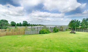 A grassy backyard with a wooden fence, a picnic table, and a view of a body of water. - 2 Bed in Waren Mill (oc-gd1324) (Waren Mill)
