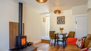 Een gezellige woonkamer met een houtkachel, een eethoek met stoelen en een tafel, en een bank met kleurrijke kussens.