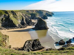 Paisagem costeira com praia de areia, falésias rochosas e o oceano.