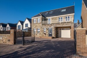 A two-story house with a stone facade, a garage, and a gated entrance. - 4 Bed in North Sunderland (oc-gd0238) (North Sunderland)