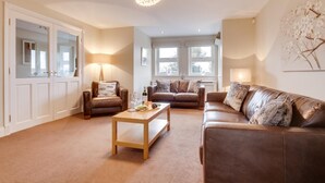 A spacious living room with a brown leather sofa, two armchairs, a wooden coffee table, and a chandelier. - 4 Bed in North Sunderland (oc-gd0238) (North Sunderland)