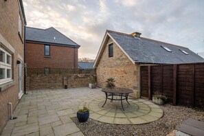 A courtyard with a patio table, potted plants, and a wooden fence. - 4 Bed in North Sunderland (oc-gd0238) (North Sunderland)