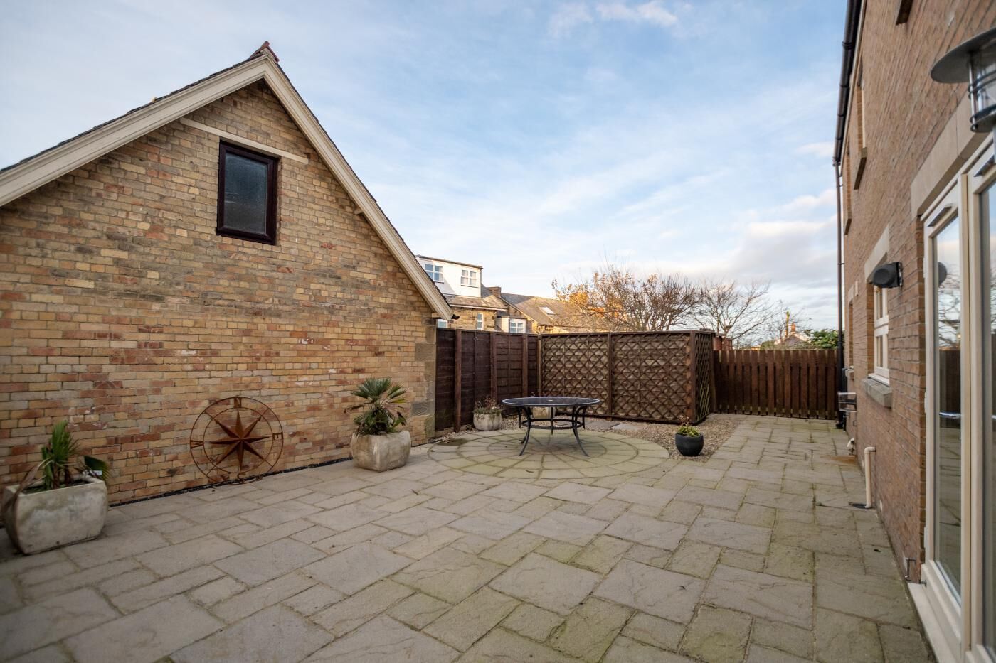 A brick building with a triangular roof, a patio with a table and chairs, and potted plants.