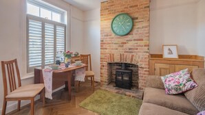 Een gezellige woonkamer met een open haard, een eethoek met een tafel en stoelen, en een bank.