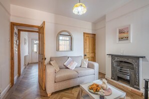 A living room with a sofa, a fireplace, and a dining table with croissants. - 2 Bed in Lowestoft (oc-c31866) (Lowestoft)