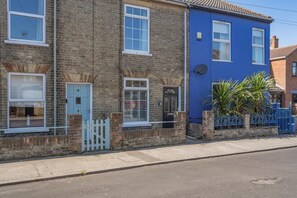 A row of terraced houses with brick and painted exteriors, a white picket fence, and a blue gate. - 2 Bed in Lowestoft (oc-c31866) (Lowestoft)