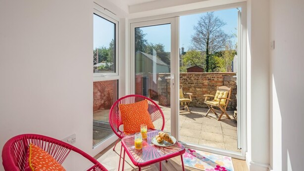 Een zonnig balkon met een tafel, stoelen en uitzicht op een tuin.