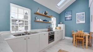 Eine moderne Küche mit Dachfenster, weißen Schränken und einem Essbereich mit Holzsesseln.