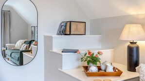 Ein modernes Wohnzimmer mit einem weißen Sofa, einem Couchtisch mit einer Teekanne und Tassen, einer Lampe und einem Bücherregal mit Büchern und Dekoration.