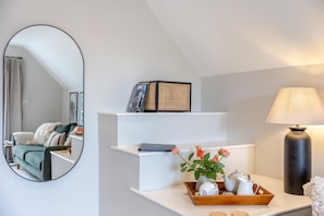 Ein modernes Wohnzimmer mit einem weißen Sofa, einem Couchtisch mit einer Teekanne und Tassen, einer Lampe und einem Bücherregal mit Büchern und Dekoration.