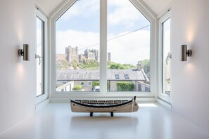 A room with a large window offering a view of a castle and surrounding buildings. - 3 Bed in Bamburgh (oc-gd0468) (Bamburgh)