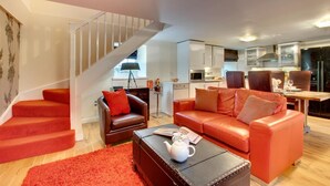 Ein modernes Wohnzimmer mit Treppe, einer Sofagarnitur und einer Küchenzeile im Hintergrund.