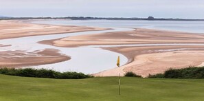 A golf course with a flagstick in the foreground and a large body of water in the background. - 2 Bed in Belford (oc-gd1023) (Adderstone with Lucker)