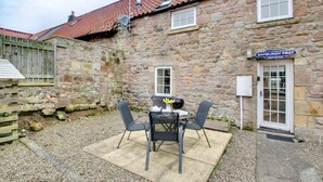 Ein Gebäude aus Stein mit einem Ziegeldach, einem Schild mit der Aufschrift 'Bamburgh First' und einer Terrasse mit Außenbestuhlung.